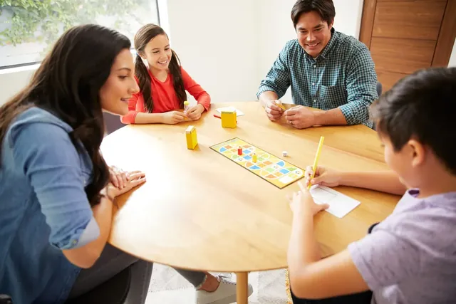 A family of four playing Pictionary at a round wooden table