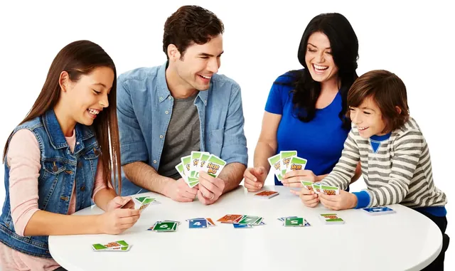 A family of four leaning over a round white table, playing Skip-Bo