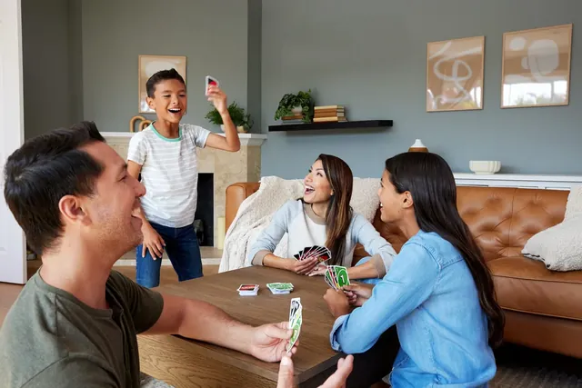 A family playing UNO in a living room, a boy jumping up as he plays a card