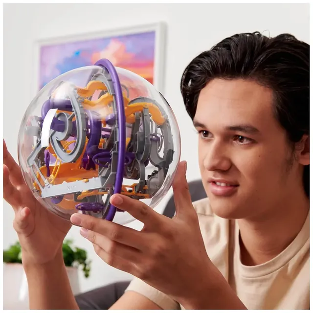 A young man holding the Perplexus Epic sphere at eye level, concentrating on the ball inside