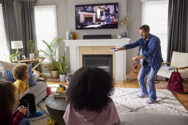 A man drawing in the air in a living room while the family watches his sketch on the TV