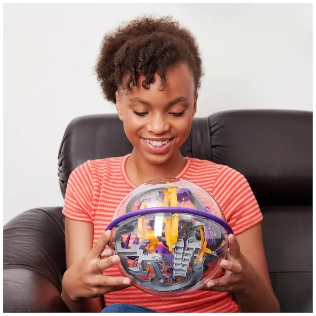 A smiling player in a striped top, sitting in an armchair and holding the Perplexus Epic sphere in both hands