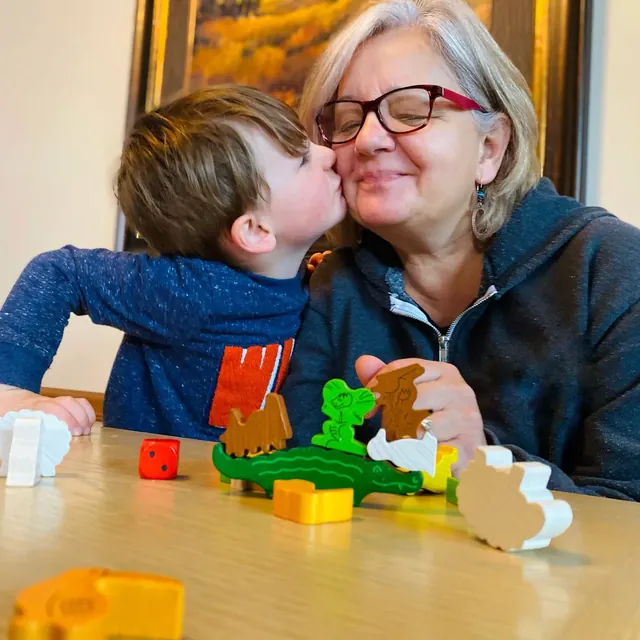 A boy kissing his grandmother's cheek beside a pile of wooden animals on the table