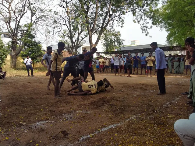 Players in a kabaddi match on a dirt ground, a raider caught by defenders while a crowd watches