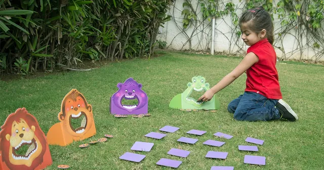 A girl kneeling on grass, feeding a card to the crocodile, seen from a distance