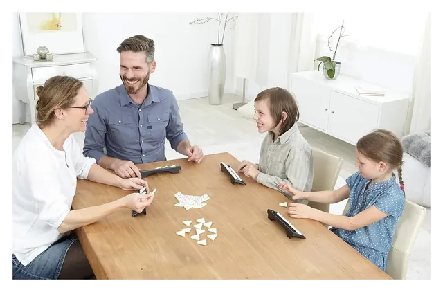 A family of four playing Triominos at a wooden table, each with a tile rack