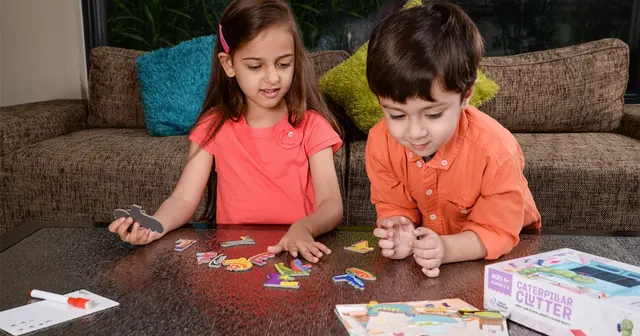 Two children at a low table picking out shoe pieces, with the box beside them, seen from a distance