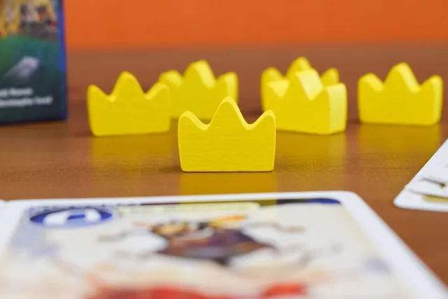 Yellow wooden crown tokens on a table beside a card