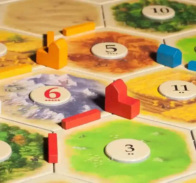 Close-up of the board: an orange and a red wooden city, wooden roads and a blue settlement sitting on terrain hexes with number tokens 5, 6, 11, 3 and 10