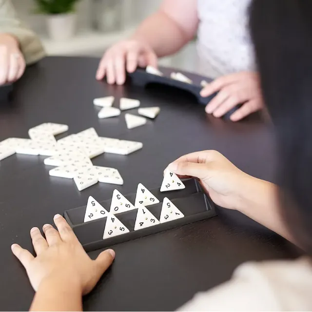 Hands placing triangular tiles on a dark table, with a rack of tiles in front