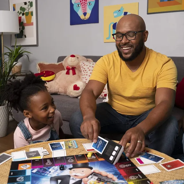 A father and daughter laughing over the Monopoly Super Electronic Banking board at home