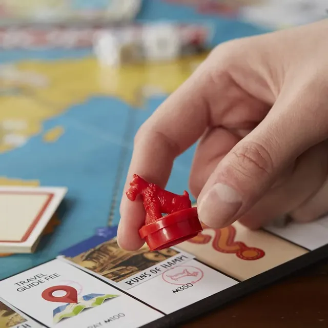 A hand moving a red stamper token past destination spaces on the board