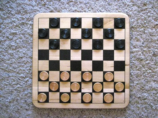 A wooden checkerboard with black and natural wooden discs set out