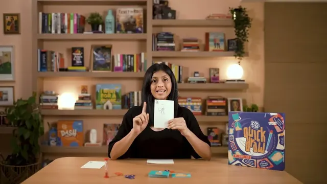 Binca's presenter at a table holding up a drawing, with the box beside her