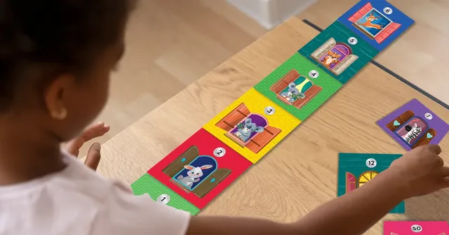 A child seen from behind, adding a floor to a long row of animal tokens on a wooden table