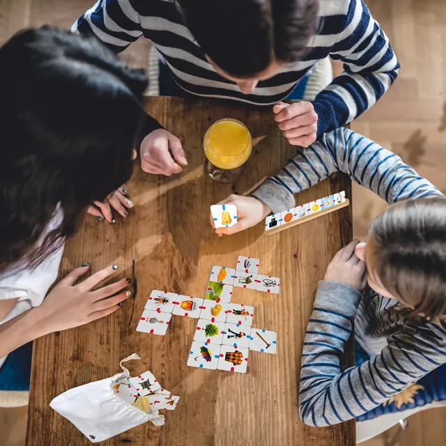 A family seen from above, playing with picture tiles on a wooden table