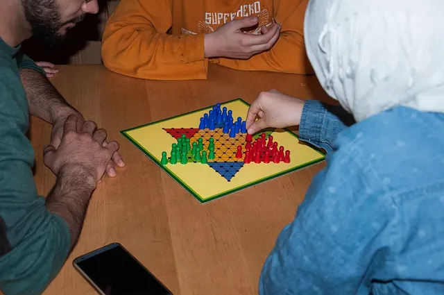 Three people around a table playing Chinese checkers on a yellow star board