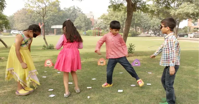 Four children playing outdoors, one in an eye mask while the others call out directions