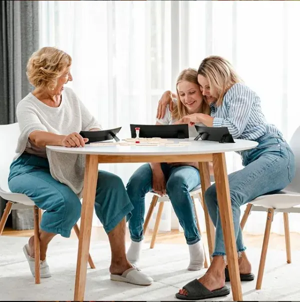 A grandmother, mother and girl playing Rummikub at a white table