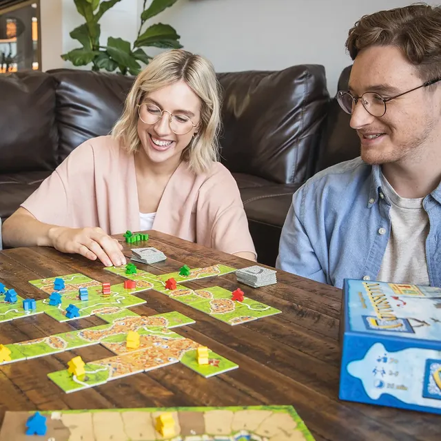 A couple smiling at a wooden table, placing tiles on a growing map