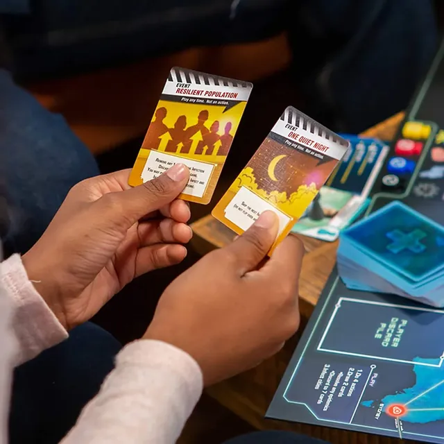A player holding city cards over the board, with the reference card and a research station nearby