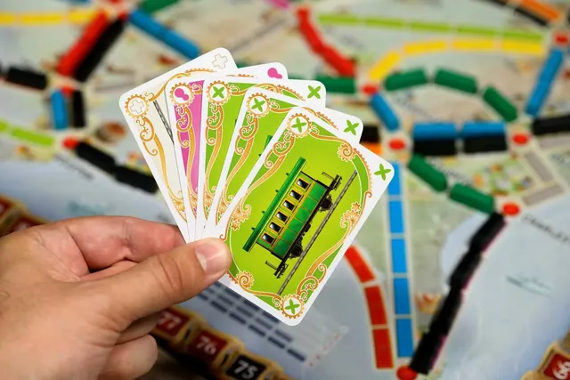 A hand holding a fan of coloured train cards over the board