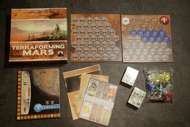 The Terraforming Mars box beside its tiles, player boards, cards and cubes