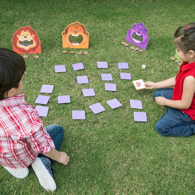 Two children on a lawn among face-down cards, with the animal stands behind them