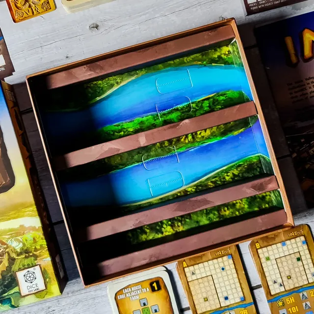 The box insert printed with a river, with map sheets and cards beside it