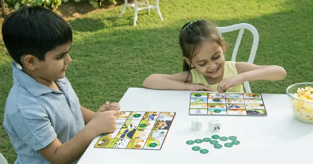 Two children playing at a garden table with boards, dice and chips, seen from a distance