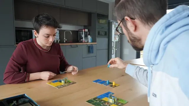 Two players leaning over their kingdoms while choosing their next domino