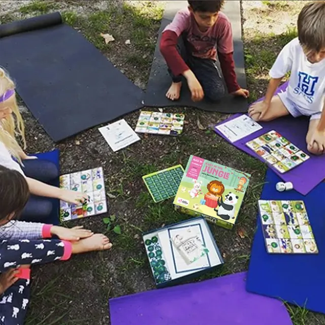 Children sitting on mats in a garden, each with a bingo board, seen from above