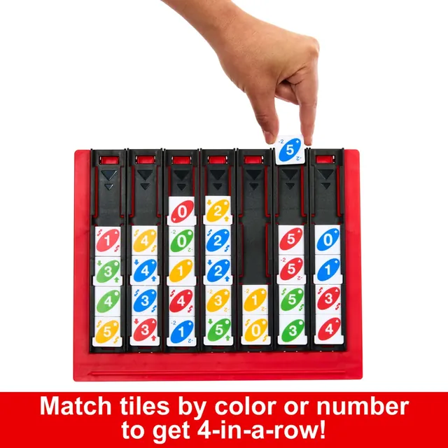 A hand dropping a blue 5 tile into one of the seven trays of a part-filled UNO Quatro grid