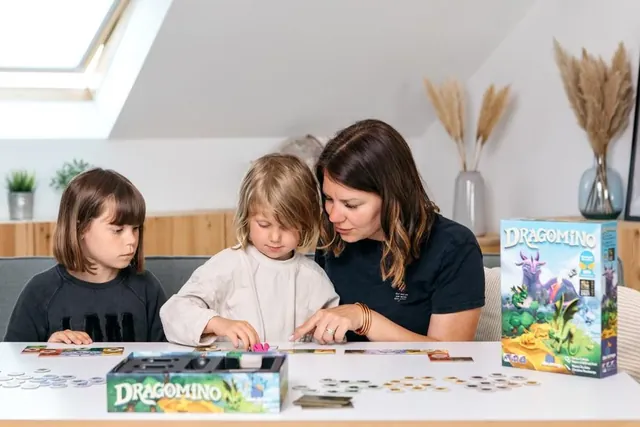 A woman and two children playing Dragomino, with the box on the table beside them