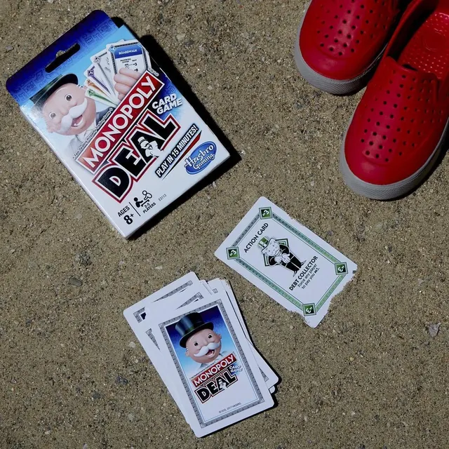 Monopoly Deal cards on the ground beside the box (English pack shown)