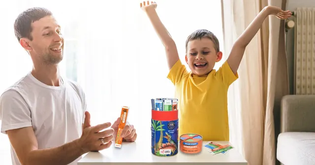 A father and son at a table, the boy cheering with his arms up beside the tube
