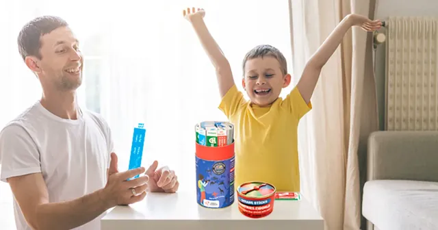 A father and son at a table, the boy cheering with his arms up beside the tube