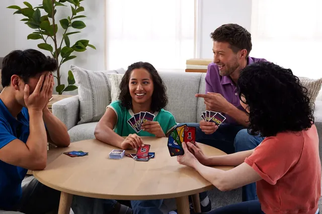 Four people around a low table playing Liar's UNO, one of them covering his face with his hand