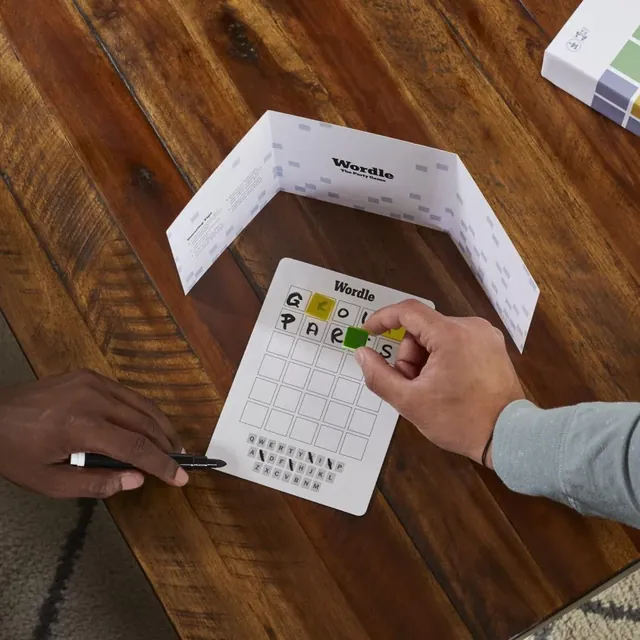 A hand placing a green tile on a player's guess on the Wordle board