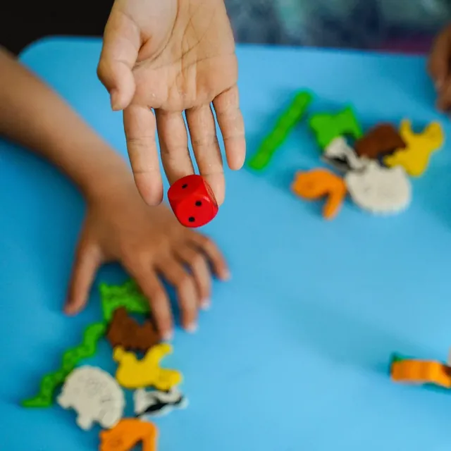 A child's hand rolling the red die over a table of wooden animals