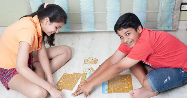 Two children on a floor, tracing paths on the boards with their fingers, seen from a distance