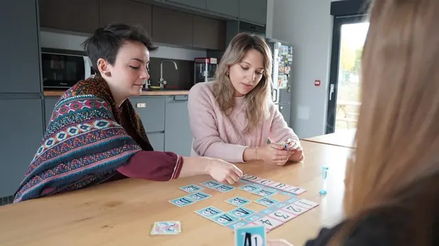 Friends at a kitchen table, one placing a clue card on the grid
