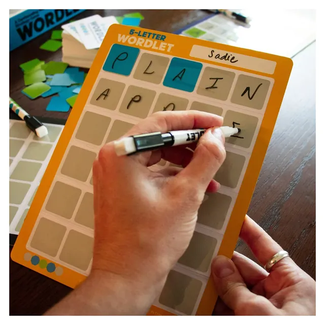 A hand writing a guess on an orange dry-erase guessing board