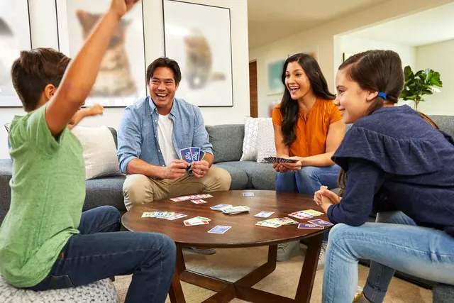 A family playing Phase 10 round a coffee table, a boy throwing his arms up in celebration
