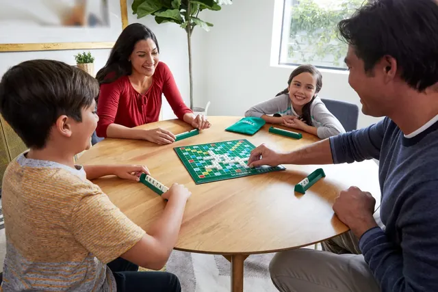 Two adults and two children playing Scrabble at a round wooden table