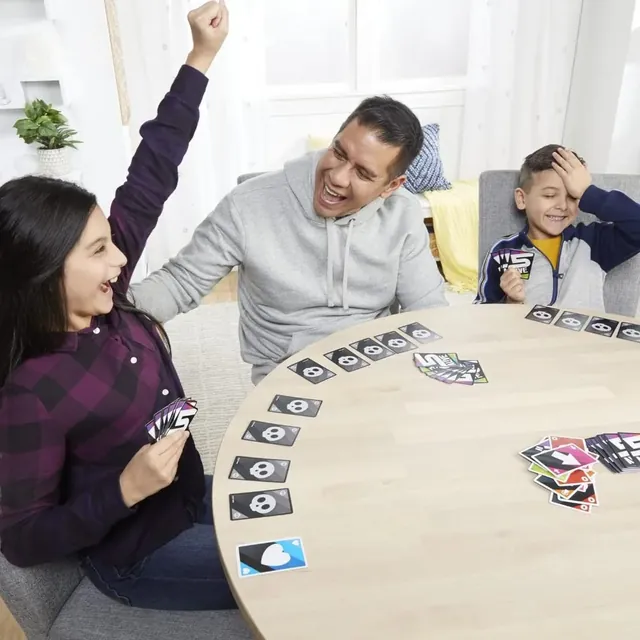 A girl throwing her arms up in triumph while a man and a boy react, at a table of 5 Alive cards